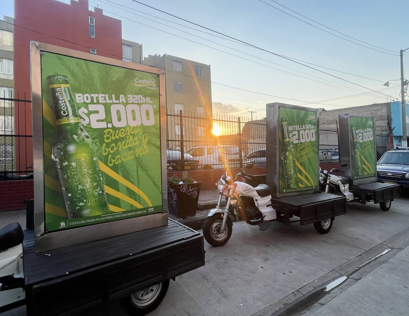 Motos valla publicitarias de cerveza costeña con piezas gráficas de bebida ubicadas fuera de la oficina en el atardecer