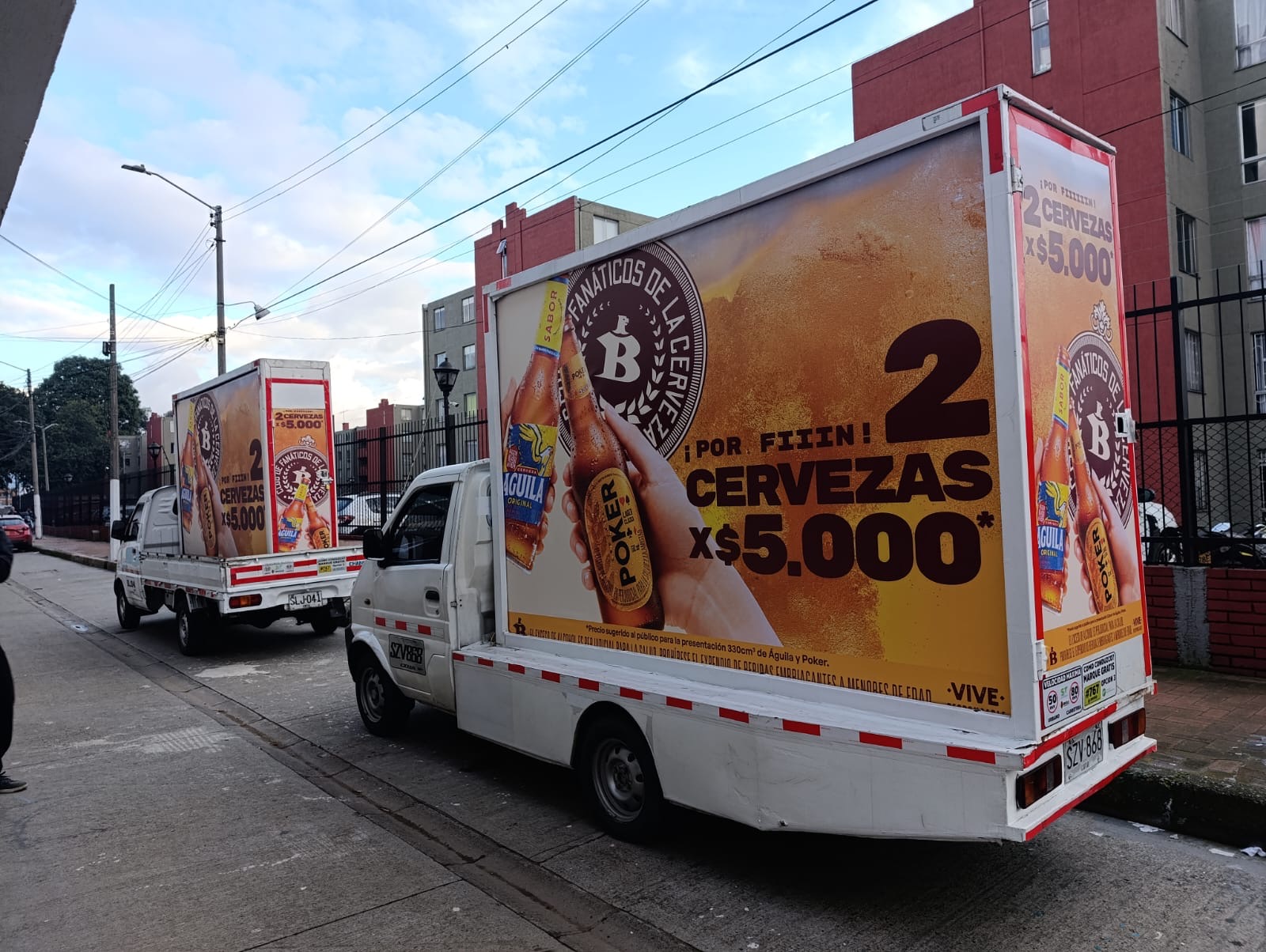 Caravana de camiones publicitarios con branding de Cerveza Poker en evento masivo